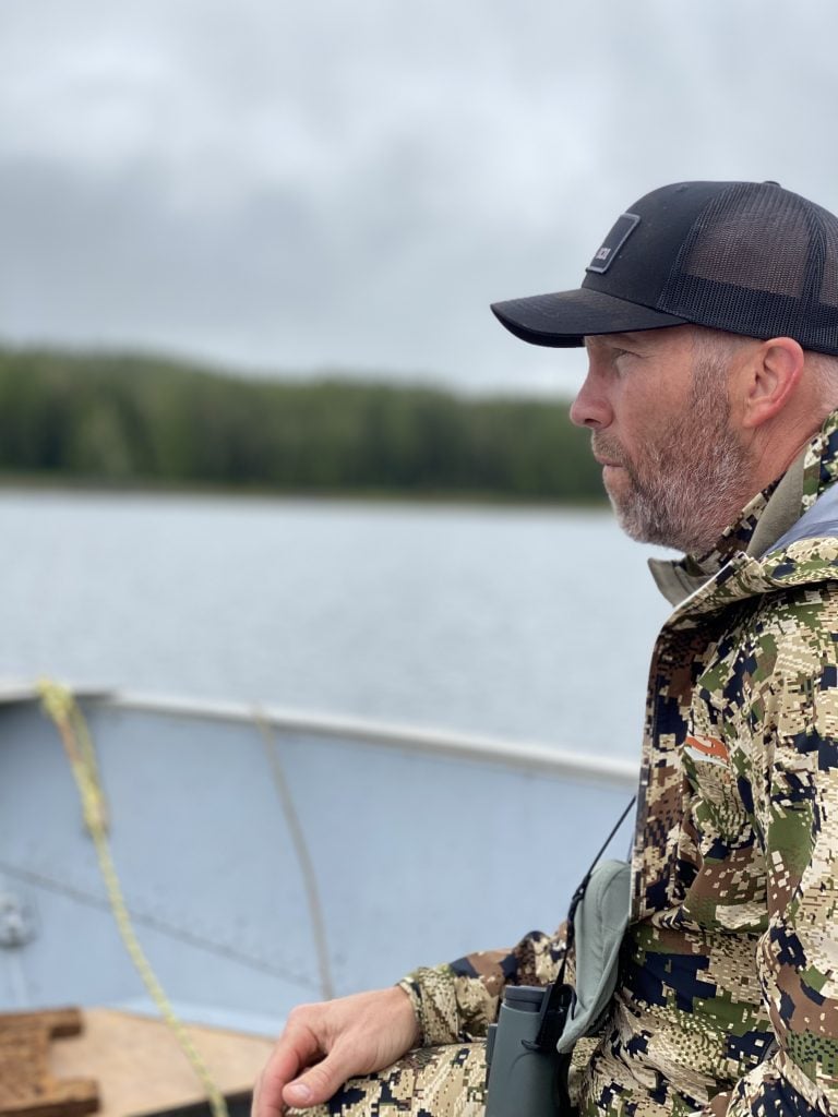 A Man in a Camouflage Suit and Cap Sits in a Boat with a Fishing